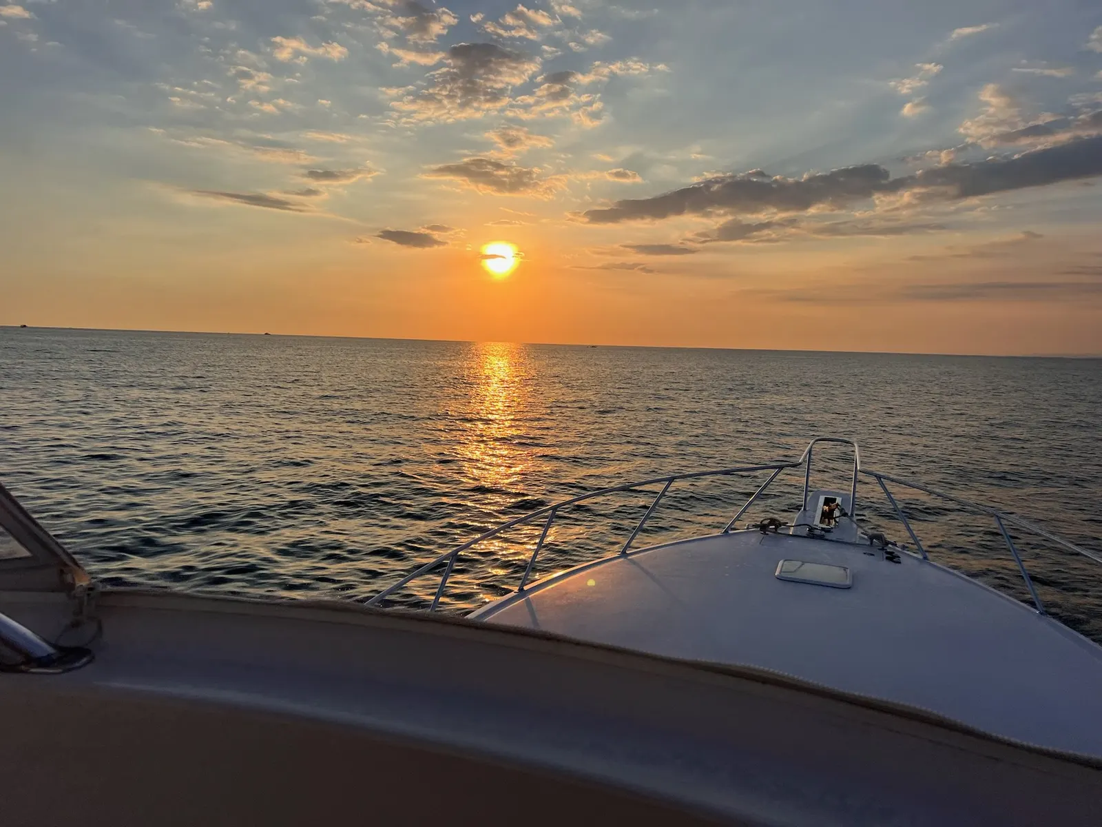 The sun low over the Pacific, laying a gold path across the water ahead of the boat’s bow rail