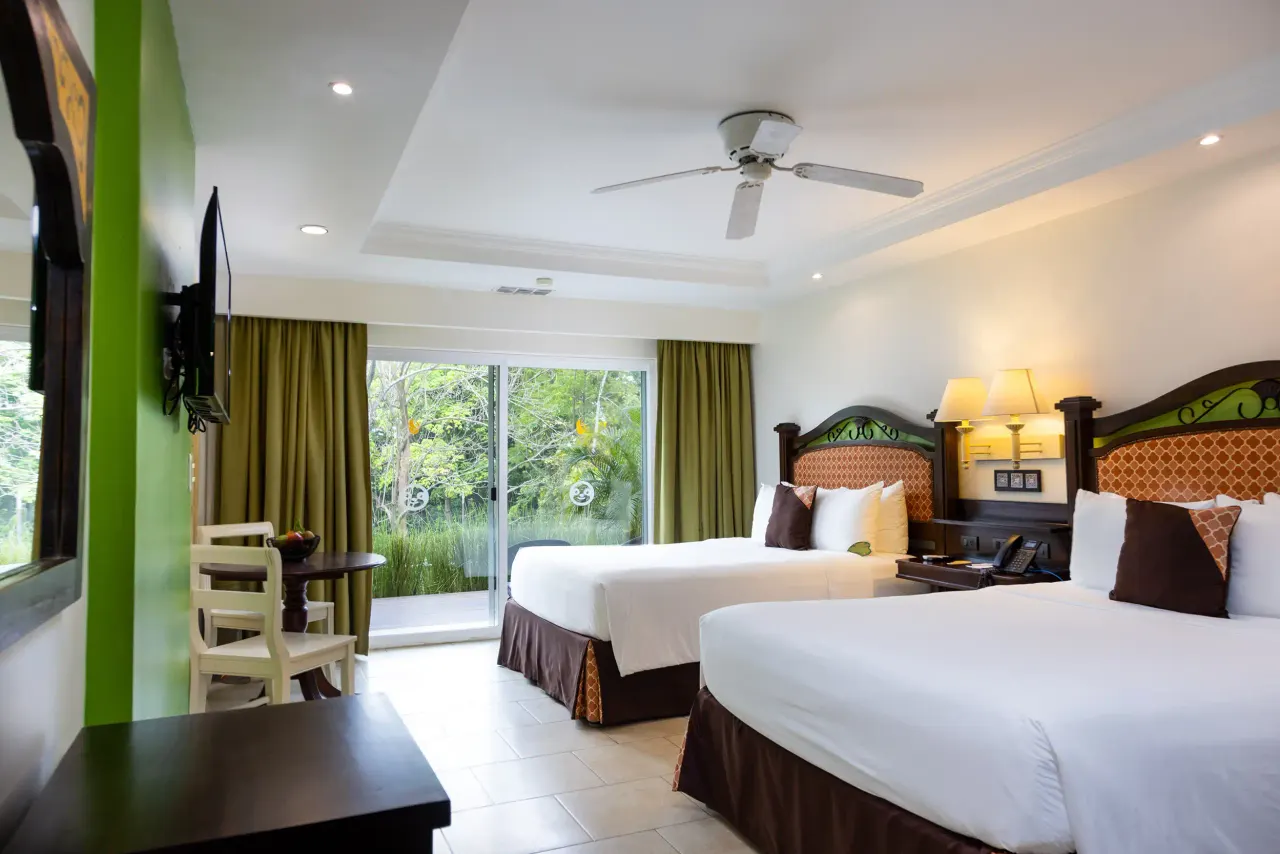 Two beds with patterned headboards and brown throws beside a sliding glass door to the garden