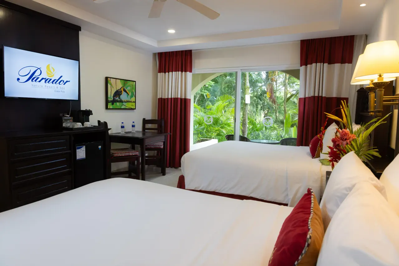 Two beds with red accents near a sliding glass door and an arched window onto palms and garden