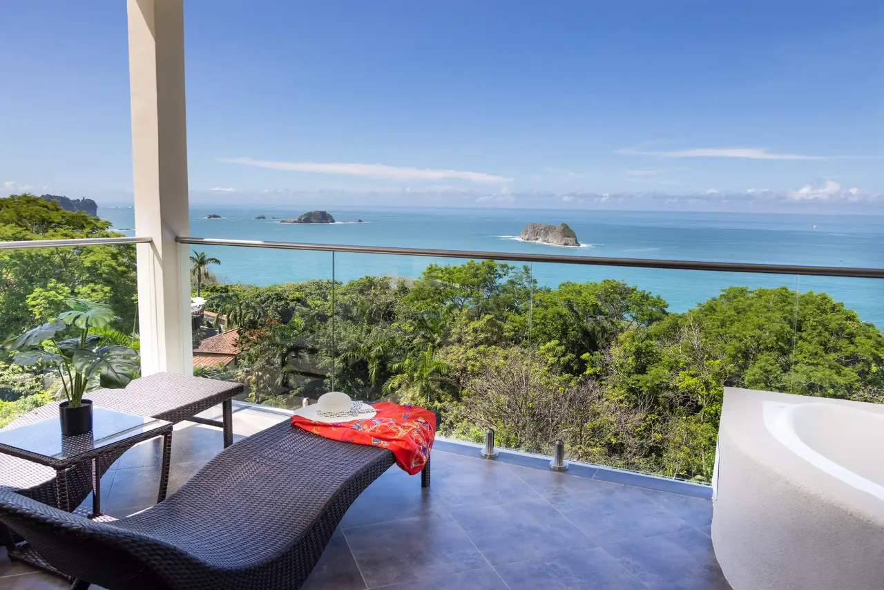 Balcony with a lounge chair, a red wrap and a sun hat, overlooking the rainforest canopy and rocky islands in the Pacific